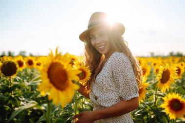 Sarı ayçiçekleriyle çevrili mutlu genç bir kadın. Çiçek bahçesinde, tatilde seyahat ediyor..