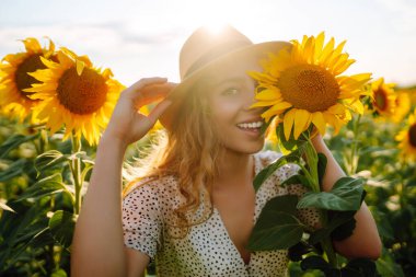 Sarı ayçiçekleriyle çevrili mutlu genç bir kadın. Çiçek bahçesinde, tatilde seyahat ediyor..