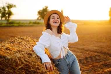 Gün batımında samanlığın yanında güzel bir kadın. Doğa, tatil, rahatlama ve yaşam tarzı.