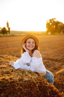 Gün batımında samanlığın yanında güzel bir kadın. Doğa, tatil, rahatlama ve yaşam tarzı.