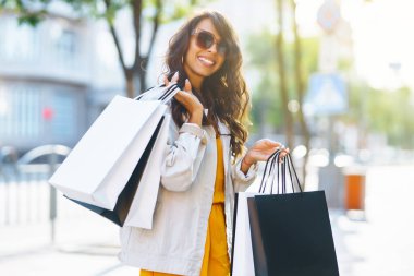 Alışveriş torbalı şık bir kadın şehrin sokaklarında yürüyor. Yaz stili. Tüketim, alım, satış, yaşam tarzı konsepti.
