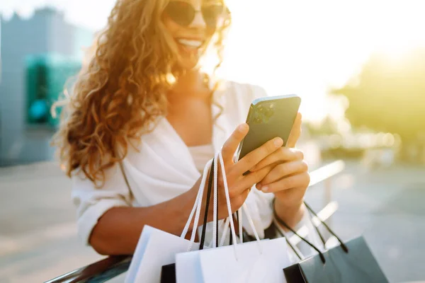 一个时髦的年轻女人在阳光灿烂的街上用电话购物 网上购物 消费主义的概念 积极的生活方式 — 图库照片