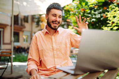 Bilgisayarı olan genç bir adam sokak kafesinde çalışıyor ya da çalışıyor. Eğitim, iş, blog veya serbest çalışma kavramı.