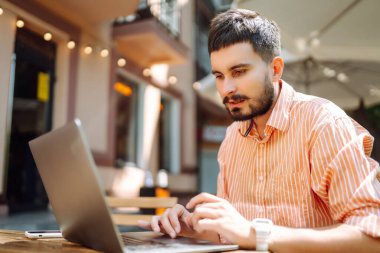 Bilgisayarı olan genç bir adam sokak kafesinde çalışıyor ya da çalışıyor. Eğitim, iş, blog veya serbest çalışma kavramı.