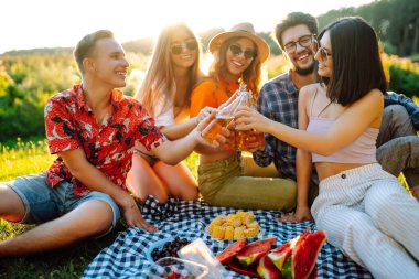 Bir grup genç, piknik için bahçede toplandı. Arkadaşlar eğlenir ve bira içerler. Tatil, piknik, arkadaşlık veya bayram konsepti.