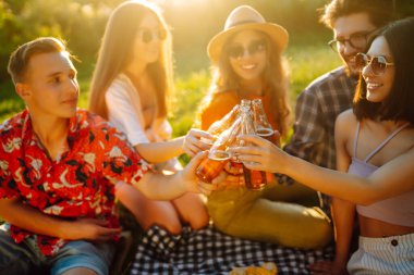 Bir grup genç, piknik için bahçede toplandı. Arkadaşlar eğlenir ve bira içerler. Tatil, piknik, arkadaşlık veya bayram konsepti.