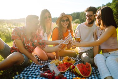 Bir grup genç, piknik için bahçede toplandı. Arkadaşlar eğlenir ve bira içerler. Tatil, piknik, arkadaşlık veya bayram konsepti.
