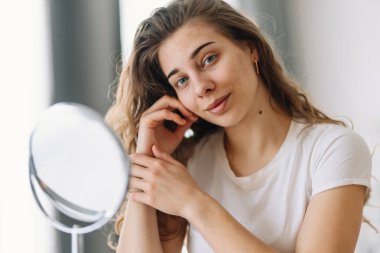 Derisi sorunlu güzel bir kadın aynaya bakıyor. Dermatoloji. Kozmetik, kırmızı nokta ya da yüzündeki kızarıklıktan kaynaklanan alerjik reaksiyon. Cilt sorunundan güzellik bakımı.