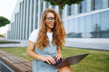 Dışarıda dizüstü bilgisayarda çalışan genç bir kadın. İş, blog yazma, serbest çalışma, eğitim kavramı.