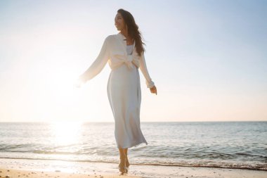 Gün batımında kumsalda yürüyen güzel bir kadın. Yaz zamanı. Seyahat, hafta sonu, rahatlama ve yaşam tarzı konsepti.