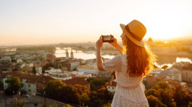 Turist kadın, şafak vakti akıllı bir telefonla şehir manzarasını vuruyor. Avrupa 'ya seyahat. Blogculuk, seyahat, turizm, teknoloji kavramı.