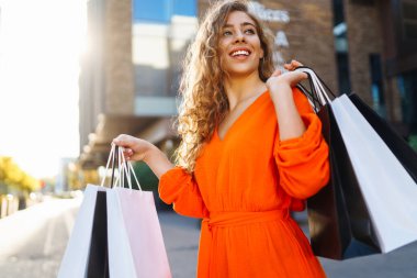 Alışveriş çantalı genç bir kadın güneşli bir cadde boyunca yürüyor. satış, alışveriş, alışveriş, yaşam tarzı konsepti, tüketim.