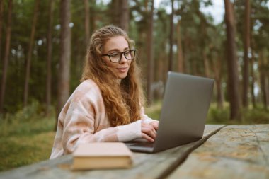 Bilgisayarlı gülümseyen genç bir kadın dışarıda çalışıyor ya da çalışıyor. İş, alışveriş, blog, çevrimiçi video konferansı.