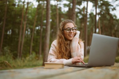 Bilgisayarlı gülümseyen genç bir kadın dışarıda çalışıyor ya da çalışıyor. İş, alışveriş, blog, çevrimiçi video konferansı.