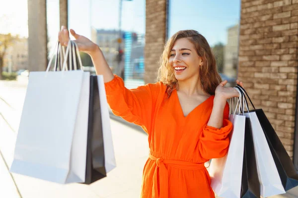 一个拿着购物袋的年轻女子沿着阳光灿烂的街道走着 生活方式概念 消费主义 — 图库照片
