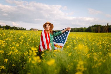 Çiçekli çayırda Amerikan bayrağı taşıyan genç bir kadın. 4 Temmuz. Bağımsızlık Günü. Vatansever bayram. ABD bayrağı rüzgarda dalgalanıyor.