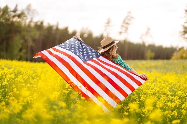 在盛开的草地上挂着美国国旗的年轻女子 7月4日独立日 爱国节假日美国国旗在风中飘扬 — 图库照片
