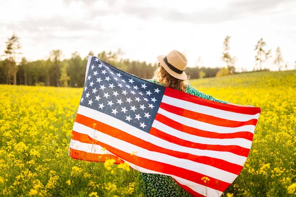 在盛开的草地上挂着美国国旗的年轻女子 7月4日独立日 爱国节假日美国国旗在风中飘扬 — 图库照片