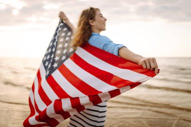 Sahilde Amerikan bayrağı taşıyan genç bir kadın. Vatansever bayram. ABD 4 Temmuz 'u kutluyor. Bağımsızlık Günü kavramı