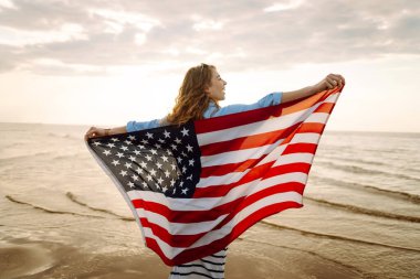 Sahilde Amerikan bayrağı taşıyan genç bir kadın. Vatansever bayram. ABD 4 Temmuz 'u kutluyor. Bağımsızlık Günü kavramı