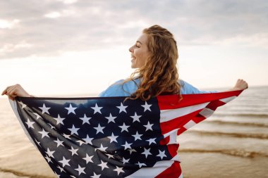 Sahilde Amerikan bayrağı taşıyan genç bir kadın. Vatansever bayram. ABD 4 Temmuz 'u kutluyor. Bağımsızlık Günü kavramı
