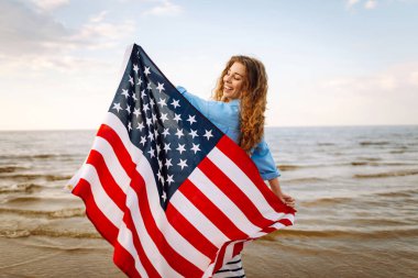 Sahilde Amerikan bayrağı taşıyan genç bir kadın. Vatansever bayram. ABD 4 Temmuz 'u kutluyor. Bağımsızlık Günü kavramı