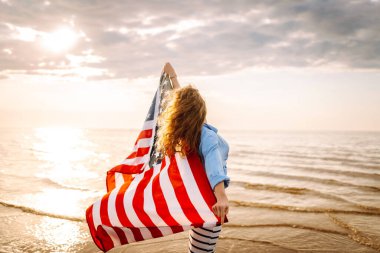 Sahilde Amerikan bayrağı taşıyan genç bir kadın. Vatansever bayram. ABD 4 Temmuz 'u kutluyor. Bağımsızlık Günü kavramı