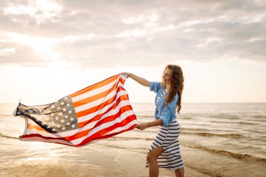 Sahilde Amerikan bayrağı taşıyan genç bir kadın. Vatansever bayram. ABD 4 Temmuz 'u kutluyor. Bağımsızlık Günü kavramı