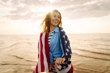 Sahilde Amerikan bayrağı taşıyan genç bir kadın. Vatansever bayram. ABD 4 Temmuz 'u kutluyor. Bağımsızlık Günü kavramı