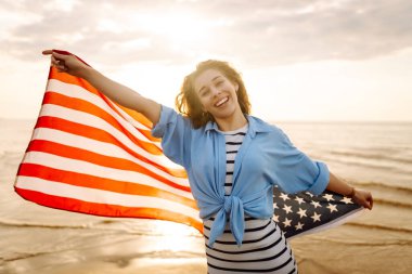 Sahilde Amerikan bayrağı taşıyan genç bir kadın. Vatansever bayram. ABD 4 Temmuz 'u kutluyor. Bağımsızlık Günü kavramı