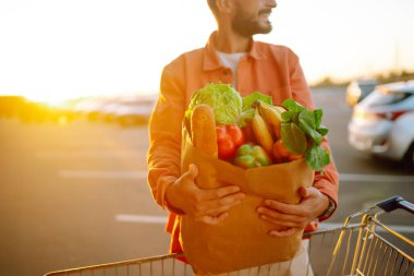 Sağlıklı yiyecekler. Sağlıklı sebzeler ve diğer yiyecek ve içeceklerle dolu bir çanta taşıyan mutlu genç adam. Tüketim, satış, alım, alışveriş, yaşam tarzı konsepti.