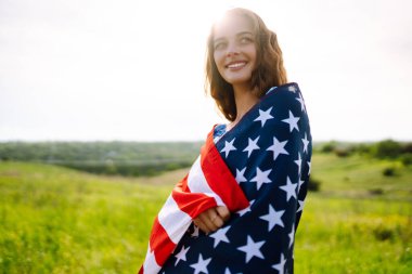 Çiçekli çayırlarda Amerikan bayrağı sallayan genç bir kadın. 4 Temmuz. Bağımsızlık Günü. Vatansever bayram. ABD bayrağı rüzgarda dalgalanıyor.