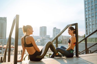 İki genç kadın sabahları dışarıda egzersiz yapıyor ve esniyor. Formda sporcular sokaklarda antrenman yapıyor olmalı. Spor, Aktif Yaşam.
