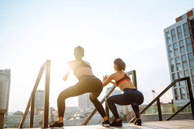 İki genç kadın sabahları dışarıda egzersiz yapıyor ve esniyor. Formda sporcular sokaklarda antrenman yapıyor olmalı. Spor, Aktif Yaşam.
