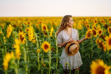 Ayçiçeği tarlasında elbise ve şapkayla poz veren güzel bir kadın. Moda, yaşam tarzı, seyahat ve tatil kavramı.