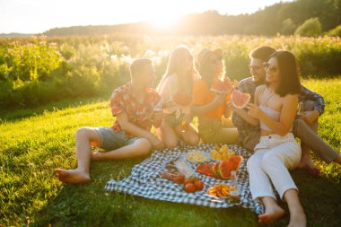Çekici, neşeli insanlar toplanıyor, toplanıyor, karpuz yiyor, piknikte boş zamanı kucaklıyor. İnsanlar, yaşam tarzı, seyahat, doğa ve tatil kavramı.