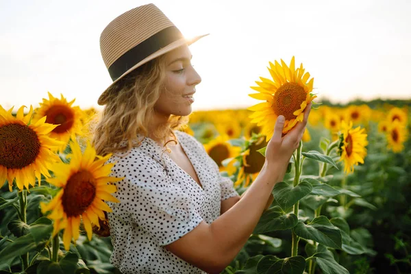 stock image Beautiful woman posing in a field of sunflowers in a dress and hat.  Fashion, lifestyle, travel and vacations concept.