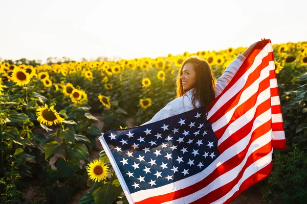 Vacker Kvinna Som Håller Amerikansk Flagga Ett Solrosfält Vid Solnedgången — Stockfoto