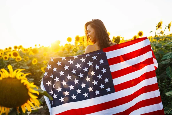 Vacker Kvinna Som Håller Amerikansk Flagga Ett Solrosfält Vid Solnedgången — Stockfoto