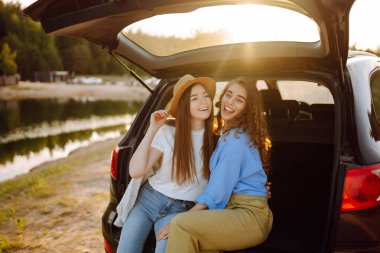 İki genç kadın yolculuk sırasında arabada selfie çekiyor. Yaşam tarzı, seyahat, turizm, doğa, aktif yaşam.