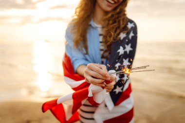 Plajda Amerikan bayrağı ve maytap taşıyan genç bir kadın. Vatansever bayram. ABD 4 Temmuz 'u kutluyor. Bağımsızlık Günü kavramı