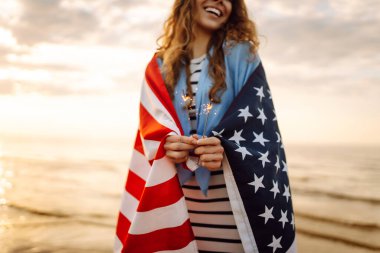 Plajda Amerikan bayrağı ve maytap taşıyan genç bir kadın. Vatansever bayram. ABD 4 Temmuz 'u kutluyor. Bağımsızlık Günü kavramı