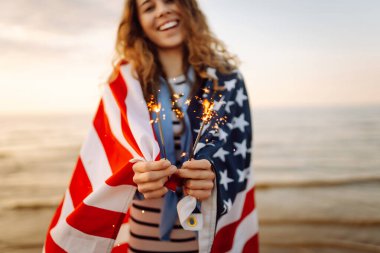 Plajda Amerikan bayrağı ve maytap taşıyan genç bir kadın. Vatansever bayram. ABD 4 Temmuz 'u kutluyor. Bağımsızlık Günü kavramı