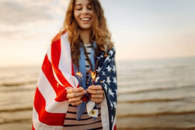 Plajda Amerikan bayrağı ve maytap taşıyan genç bir kadın. Vatansever bayram. ABD 4 Temmuz 'u kutluyor. Bağımsızlık Günü kavramı