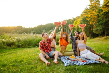 Açık havada piknikte karpuz yiyen gençler. İnsanlar, yaşam tarzı, seyahat, doğa ve tatil kavramı.