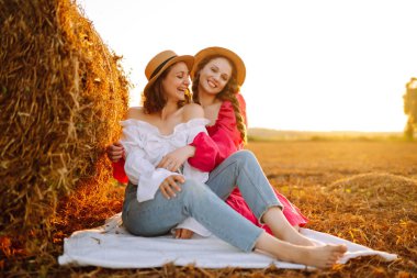Saman balyalarının yanındaki buğday tarlasında poz veren iki kadın. Doğa, tatil, rahatlama ve yaşam tarzı. Yaz manzarası.