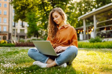 Bilgisayarlı gülümseyen genç bir kadın dışarıda çalışıyor ya da çalışıyor. Eğitim, iş, blog veya serbest çalışma kavramı.