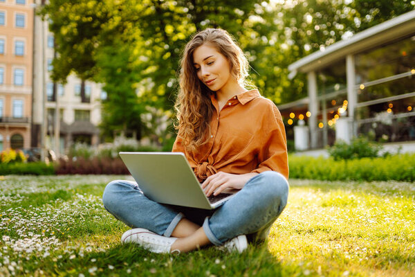 Smiling young woman with a laptop working or studying online outdoor. Concept for education, business, blog or freelance.