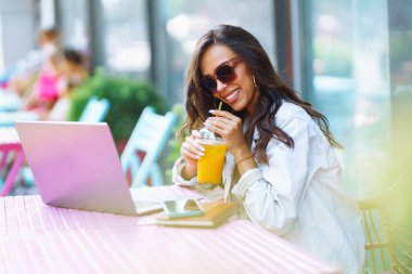 Kafede oturan ve dizüstü bilgisayar kullanan genç bir kadın. Eğitim kavramı, çevrimiçi, serbest, iş.