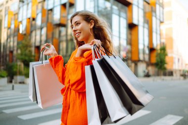 Alışveriş torbalı şık bir kadın şehrin sokaklarında yürüyor. Tüketim, satın alma, alışveriş, yaşam tarzı konsepti.